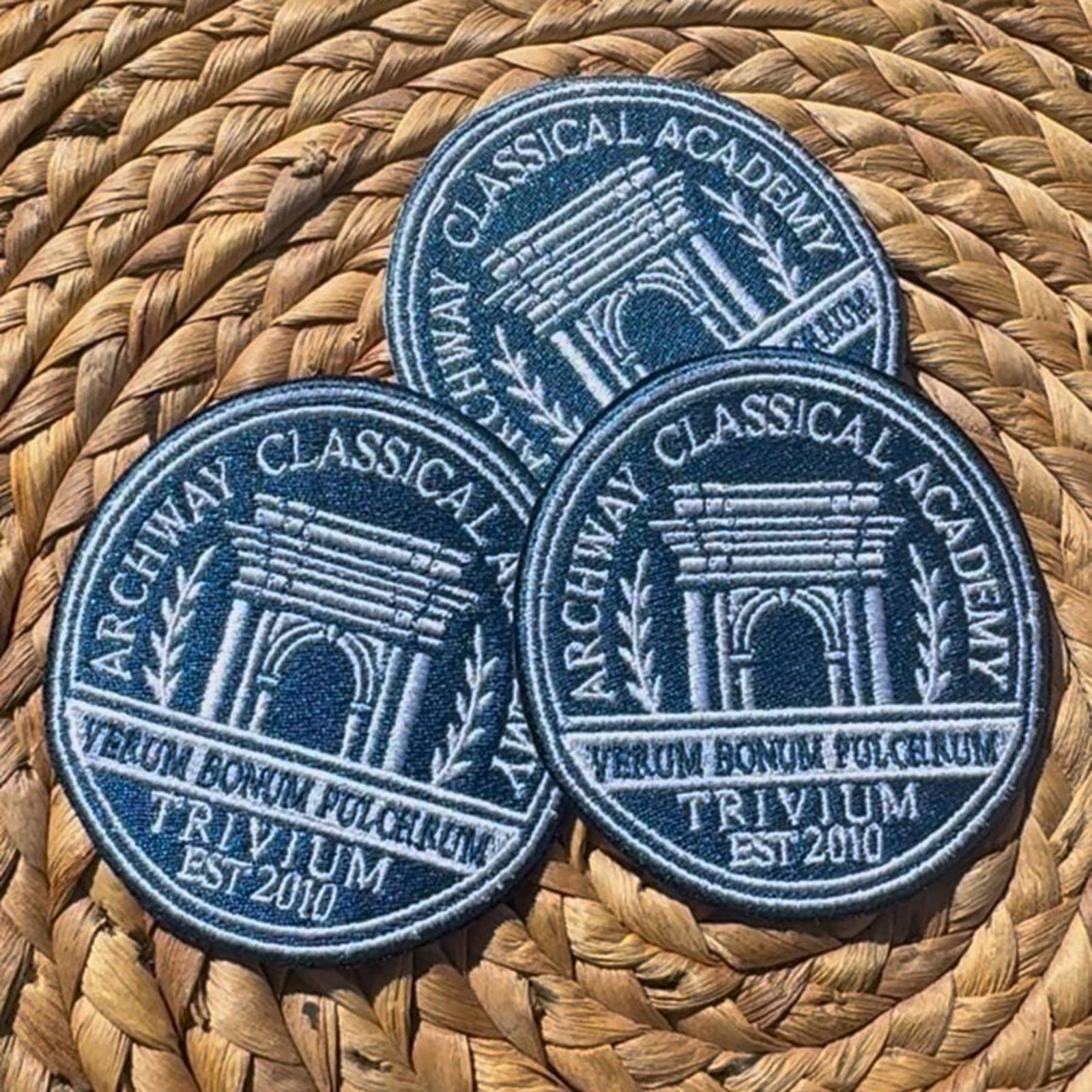 Three custom embroidered patches with a blue and white design, placed on a woven basket.