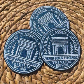 Three custom embroidered patches with a blue and white design, placed on a woven basket.