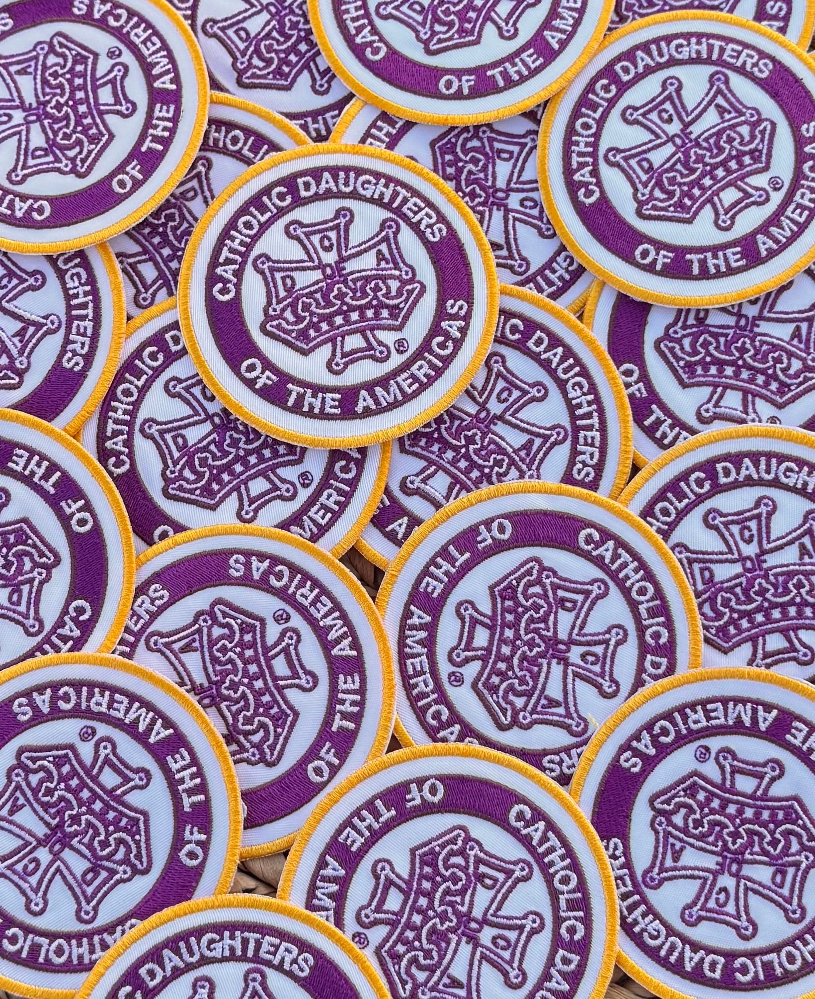 A collection of custom embroidered patches with a purple and yellow design and text that reads 'Catholic Daughters of the Americas.'.