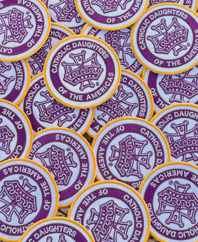 A collection of custom embroidered patches with a purple and yellow design and text that reads 'Catholic Daughters of the Americas.'.