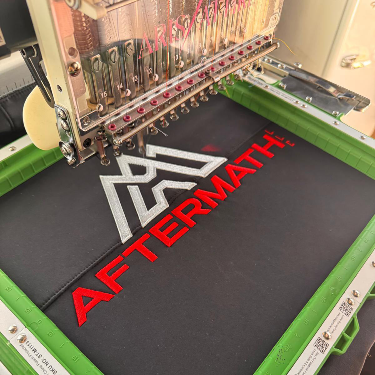 Embroidery machine stitching the aftermath logo in red and white thread