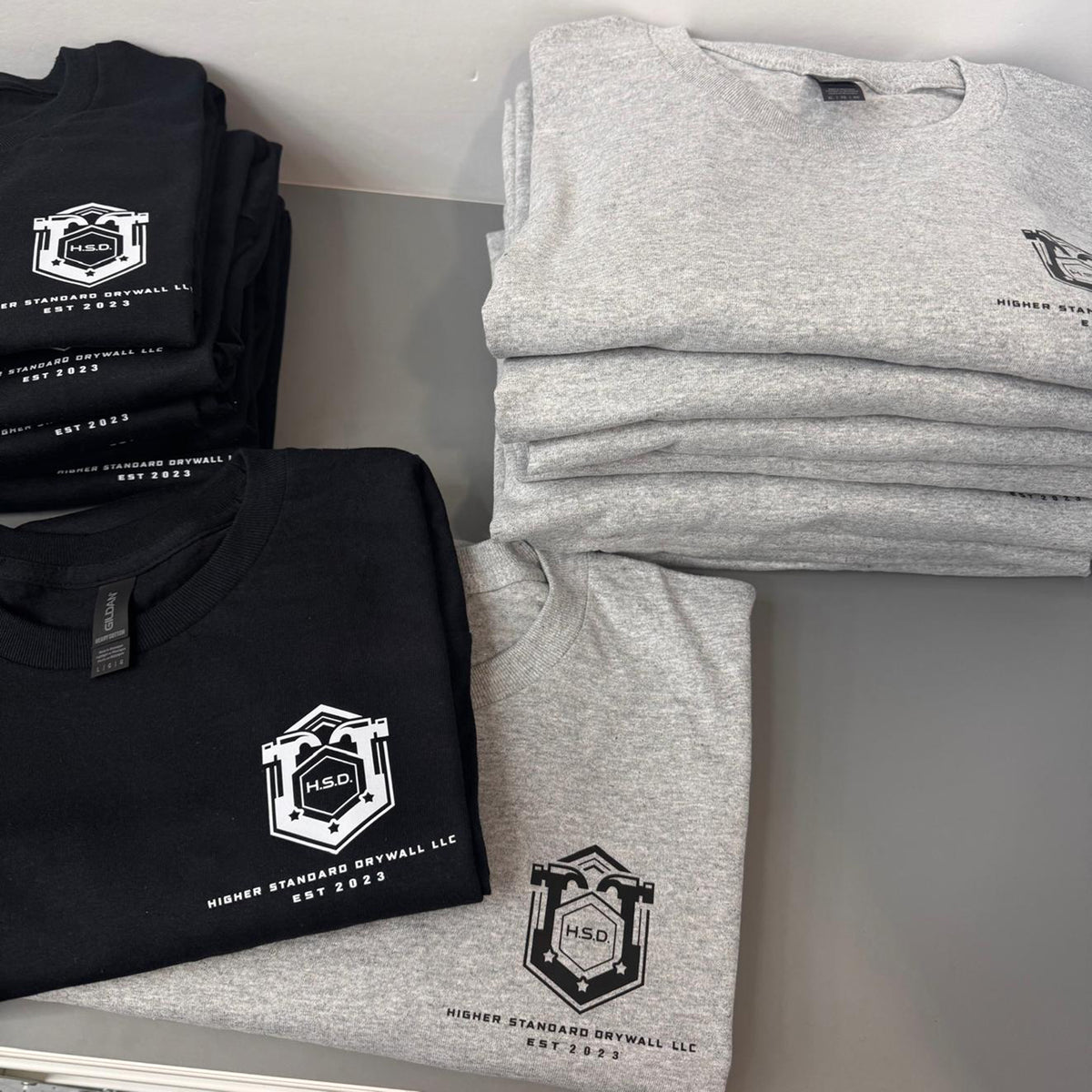 folded black and gray Tshirts printed with direct to film with the Higher Standard Drywall LLC logo