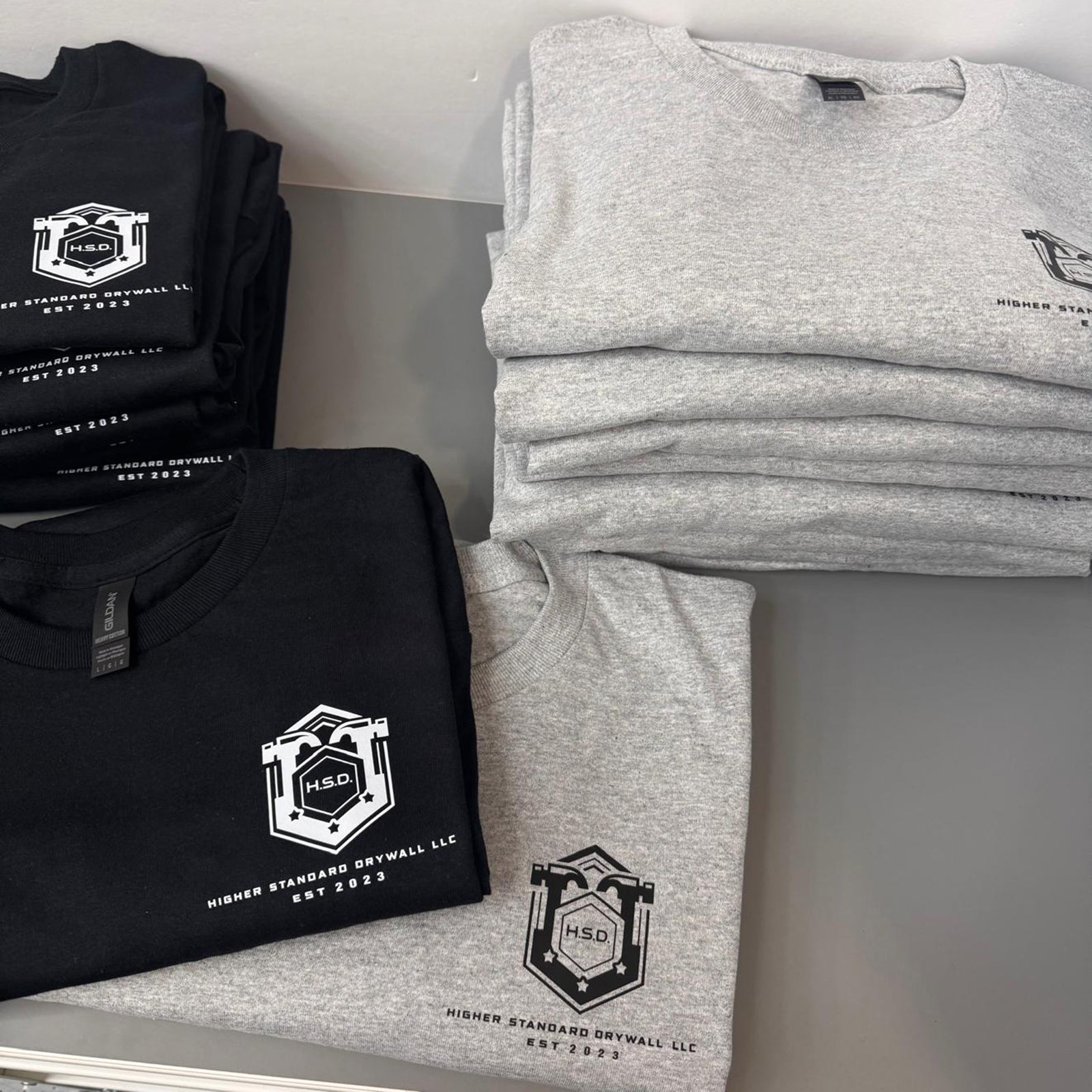 folded black and gray Tshirts printed with direct to film with the Higher Standard Drywall LLC logo